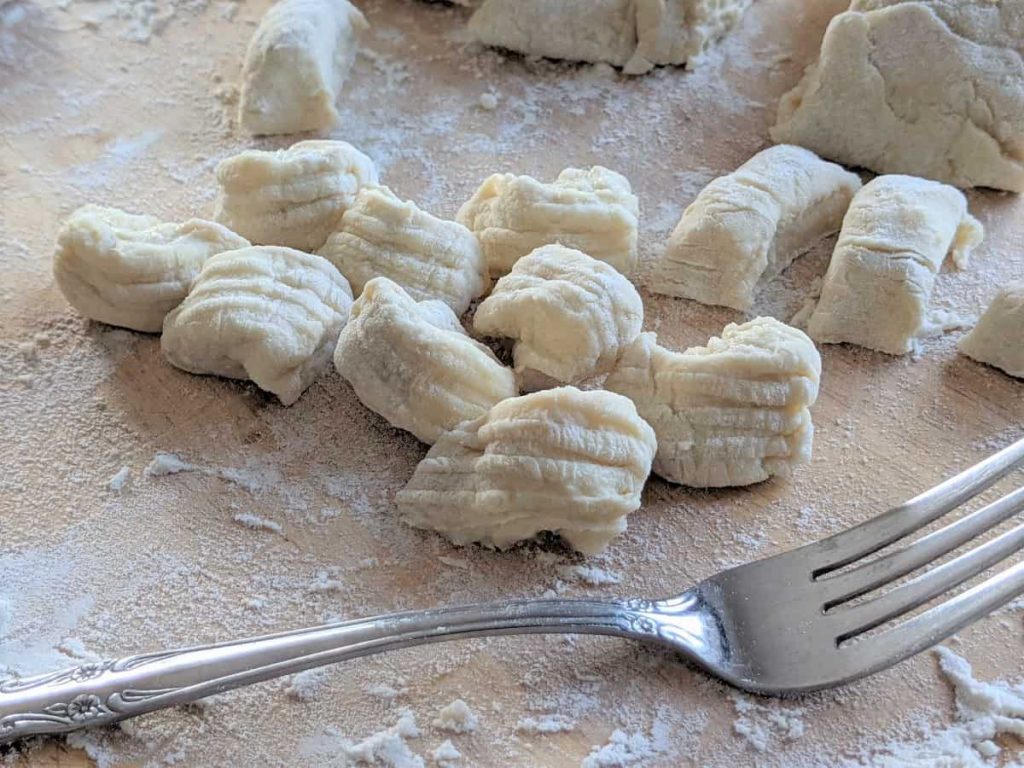 scored gnocchi dough on a cutting board with a fork