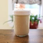 Homemade oat milk in a glass jar with a white lid on a wooden table.