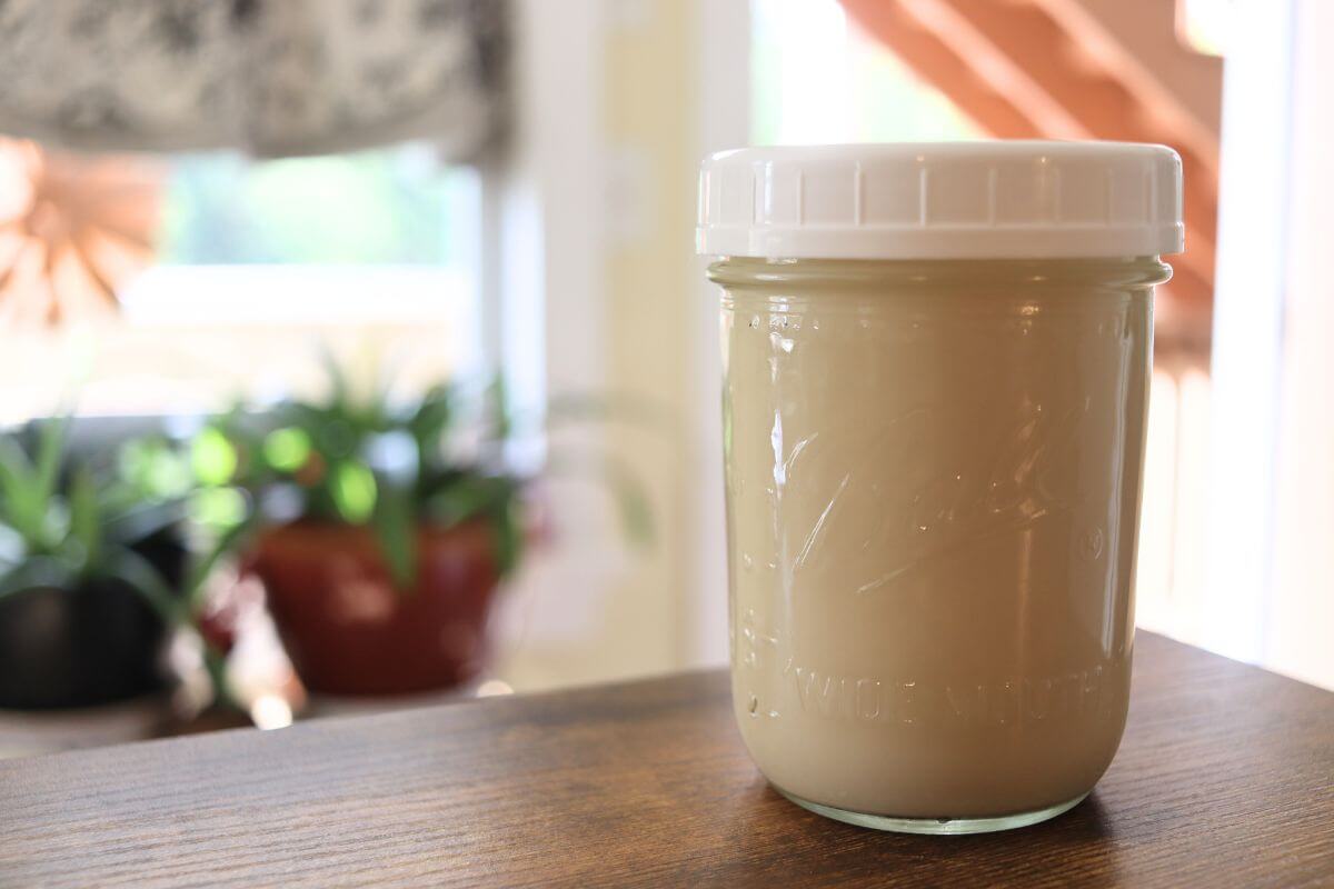Glass jar filled with homemade oat milk on a wooden table.