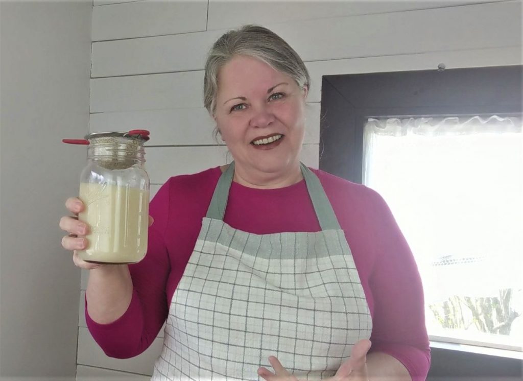 woman holding a mason jar of homemade oat milk with a strainer on top