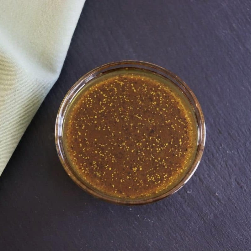 A glass bowl filled with a dark brown liquid that has spices visible in it sits on a dark surface next to a light green cloth.
