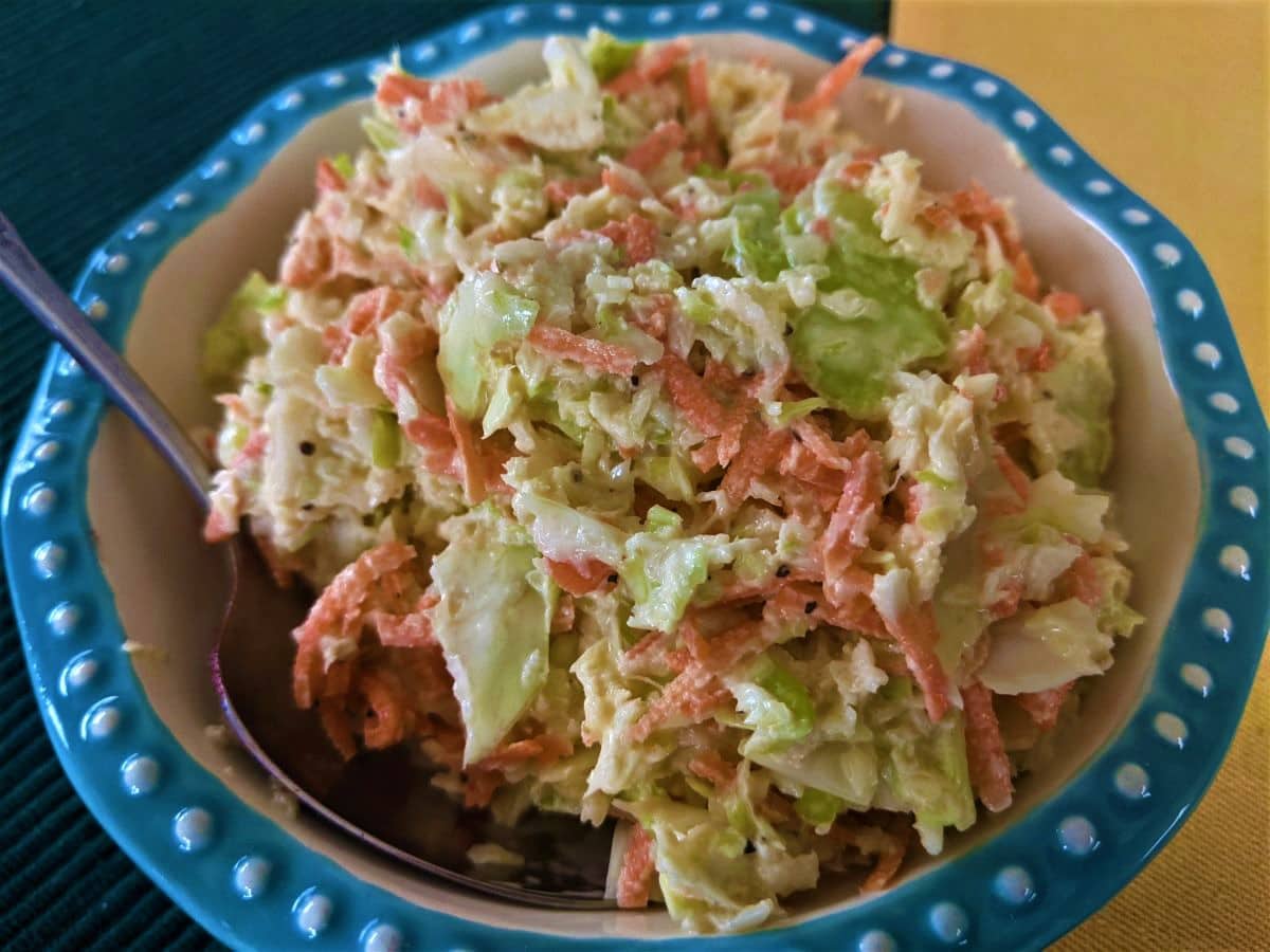 Sliced cabbage and carrots in a creamy sauce in a bowl with a blue rim.