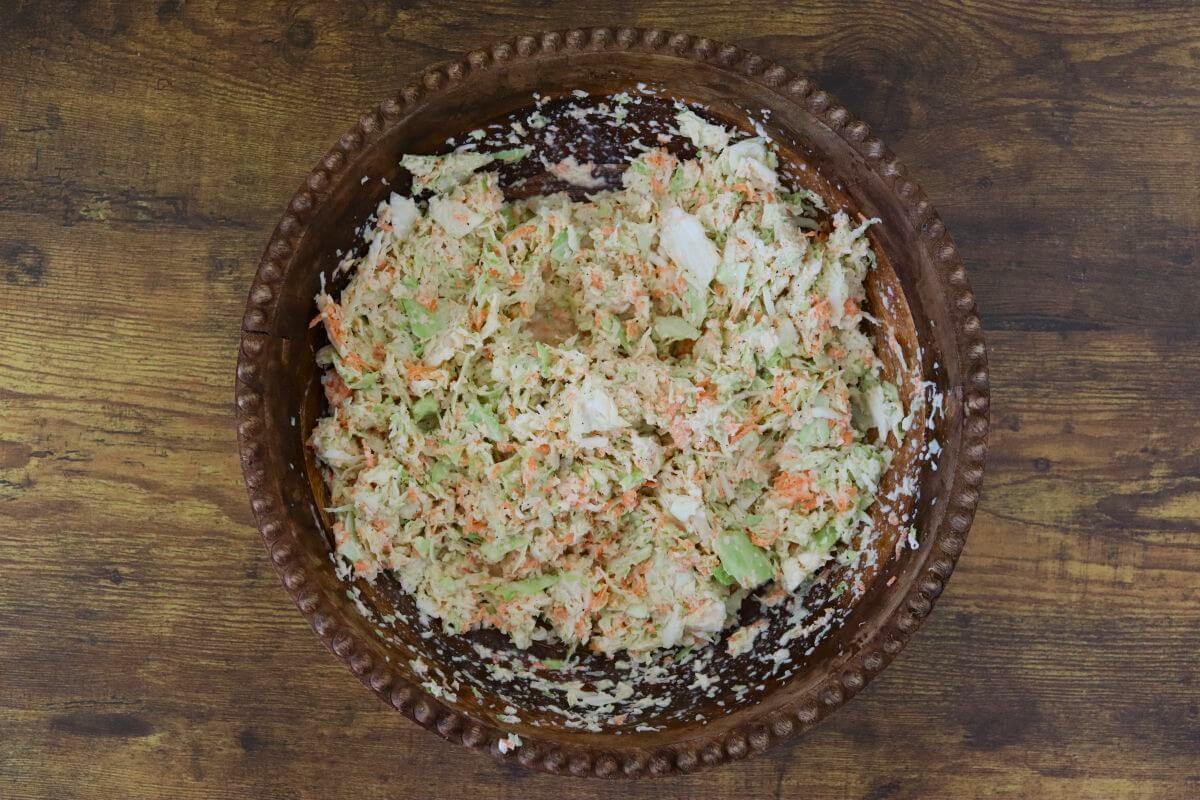 Mixed grated cabbage and carrots in a wooden bowl with evenly coated in dressing.