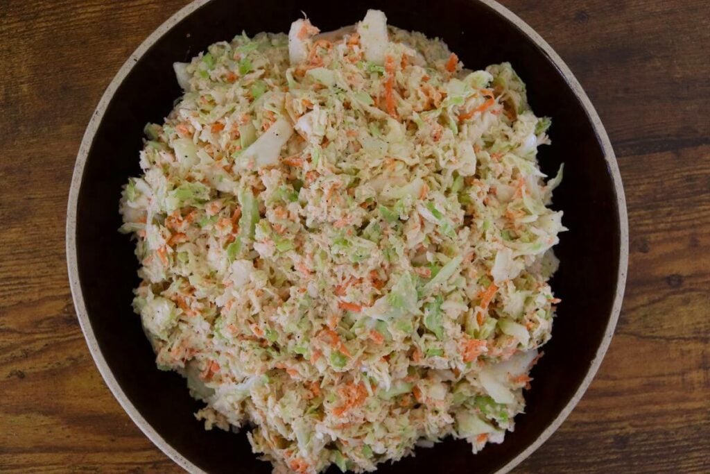 Bowl of finely grated cabbage and carrot coleslaw on a wooden table.