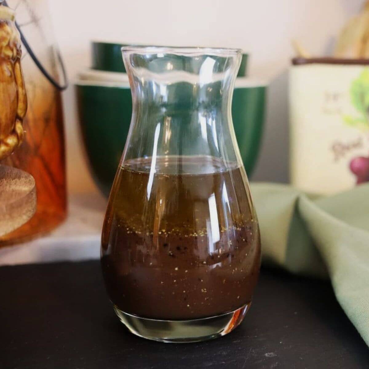 Balsamic mustard dressing in a clear glass carafe on a dark kitchen counter.
