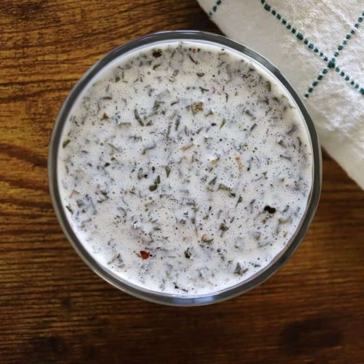 Dill dressing in a small glass bowl on a countertop with a green and white cloth next to it.