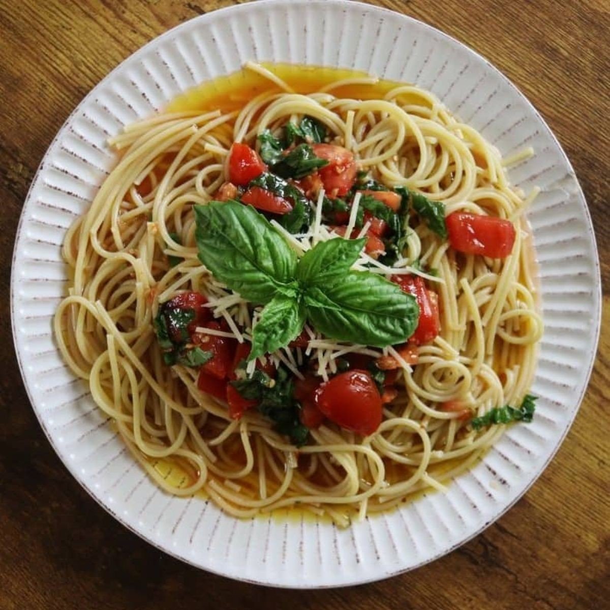 Plate of spaghetti topped with chopped tomatoes, fresh basil, and oil and garnished with a sprig of fresh basil leaves.