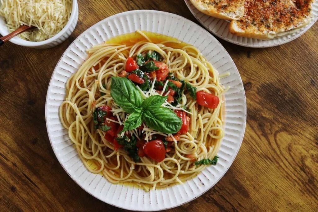 Linguine topped with tomatoes, basil, and an olive oil sauce on a white plate.
