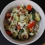 White dish with chopped zucchini and tomatoes topped with shredded cheese in it.