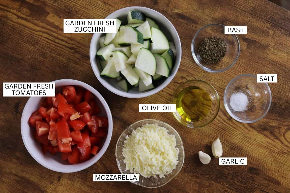 Bowls containing chopped zucchini, chopped tomatoes, shredded mozzarella, olive oil, dried basil, salt, and two garlic cloves, each ingredient labeled with text.