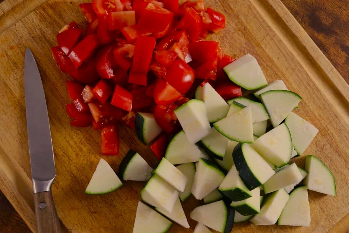 Cut zucchini and tomatoes on a cutting board with a knife.