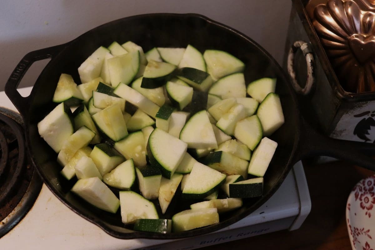 Cut up zucchini in a cast iron skillet on a stovetop with kitchen decor visible next to it.