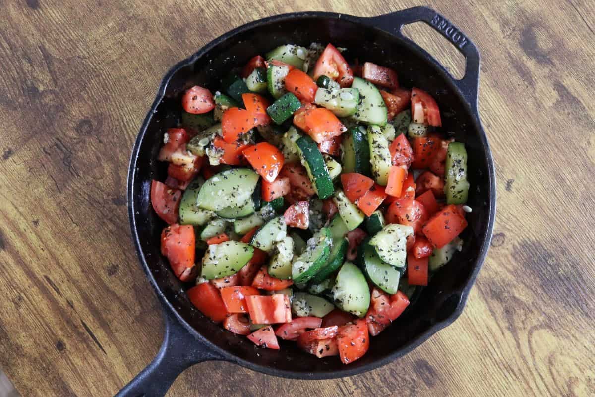 Cast iron skillet full of seasoned zucchini and tomatoes on a wooden countertop.