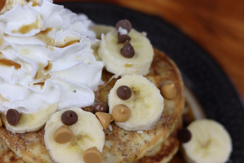 bananas, chocolate chips, and whipped cream on a stack of gluten free pancakes