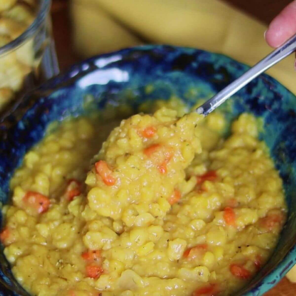 Spoon scooping yellow split pea soup with visible carrots from blue ceramic bowl.