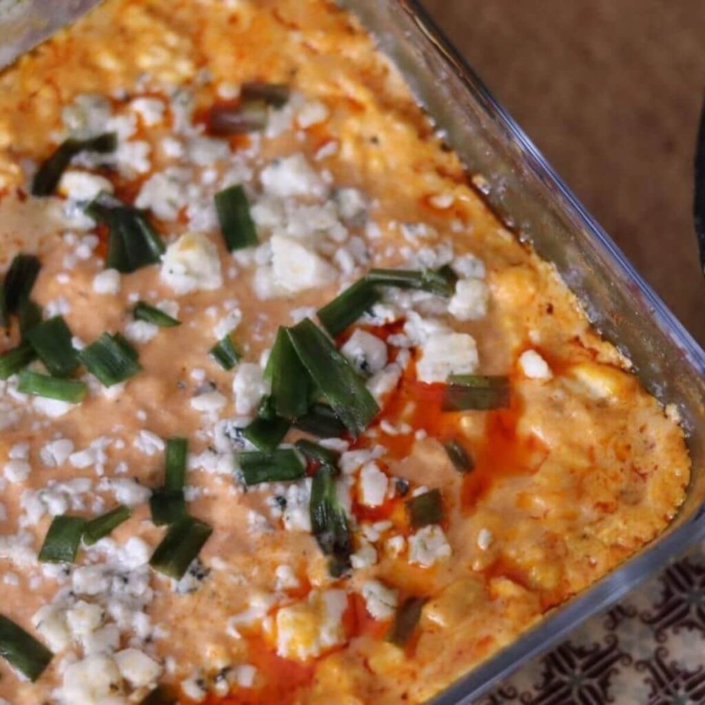 Baked buffalo chicken dip in square glass pan with melted top, blue cheese crumbles, and green onions.