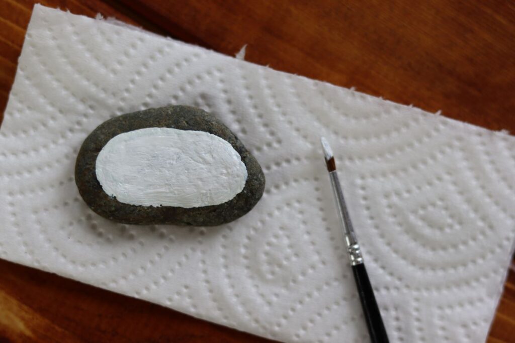 white oval painted on a stone with a paintbrush