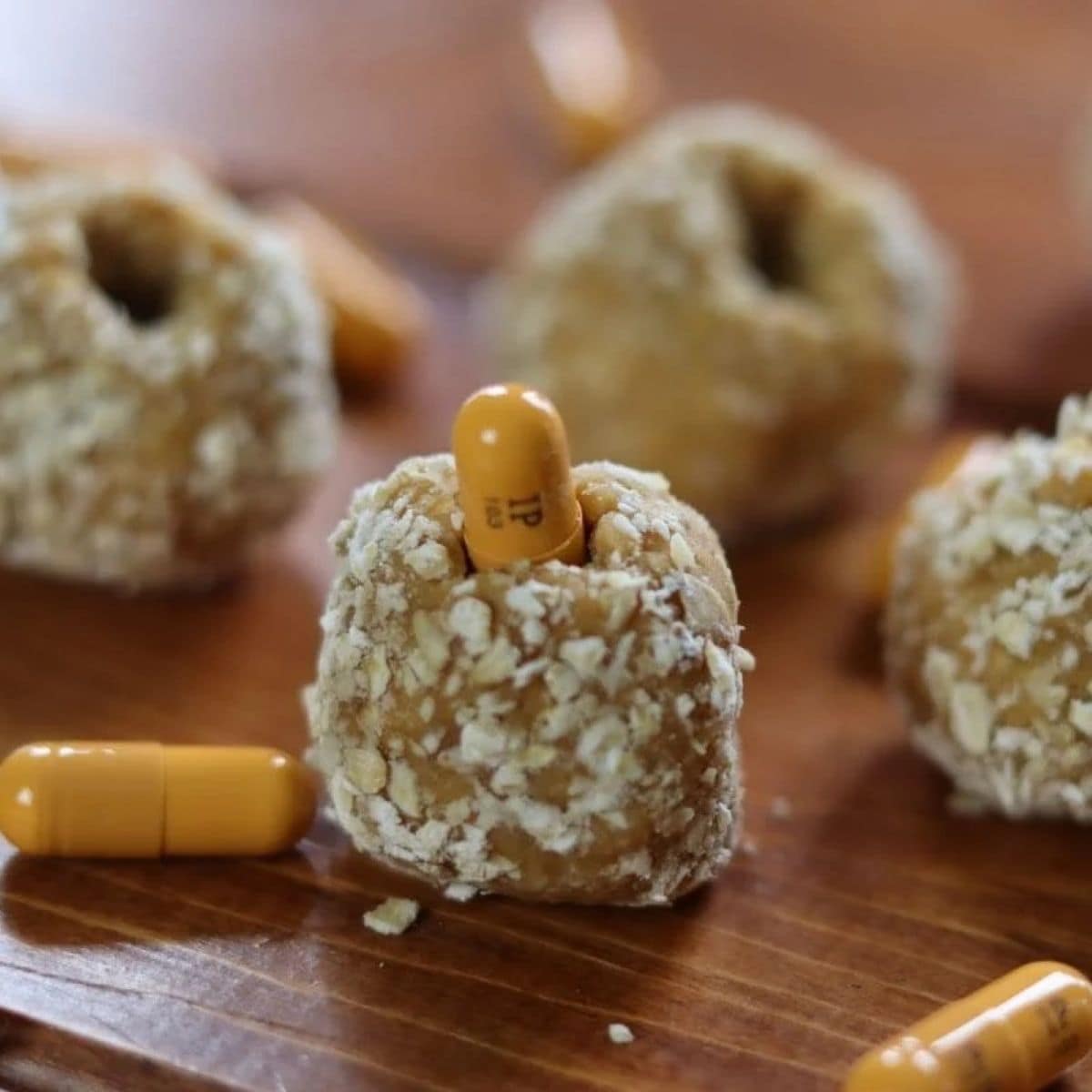 Pill pocket for dogs with a yellow pill sticking out the top of it and other pill pockets and pills scattered on the table around it.