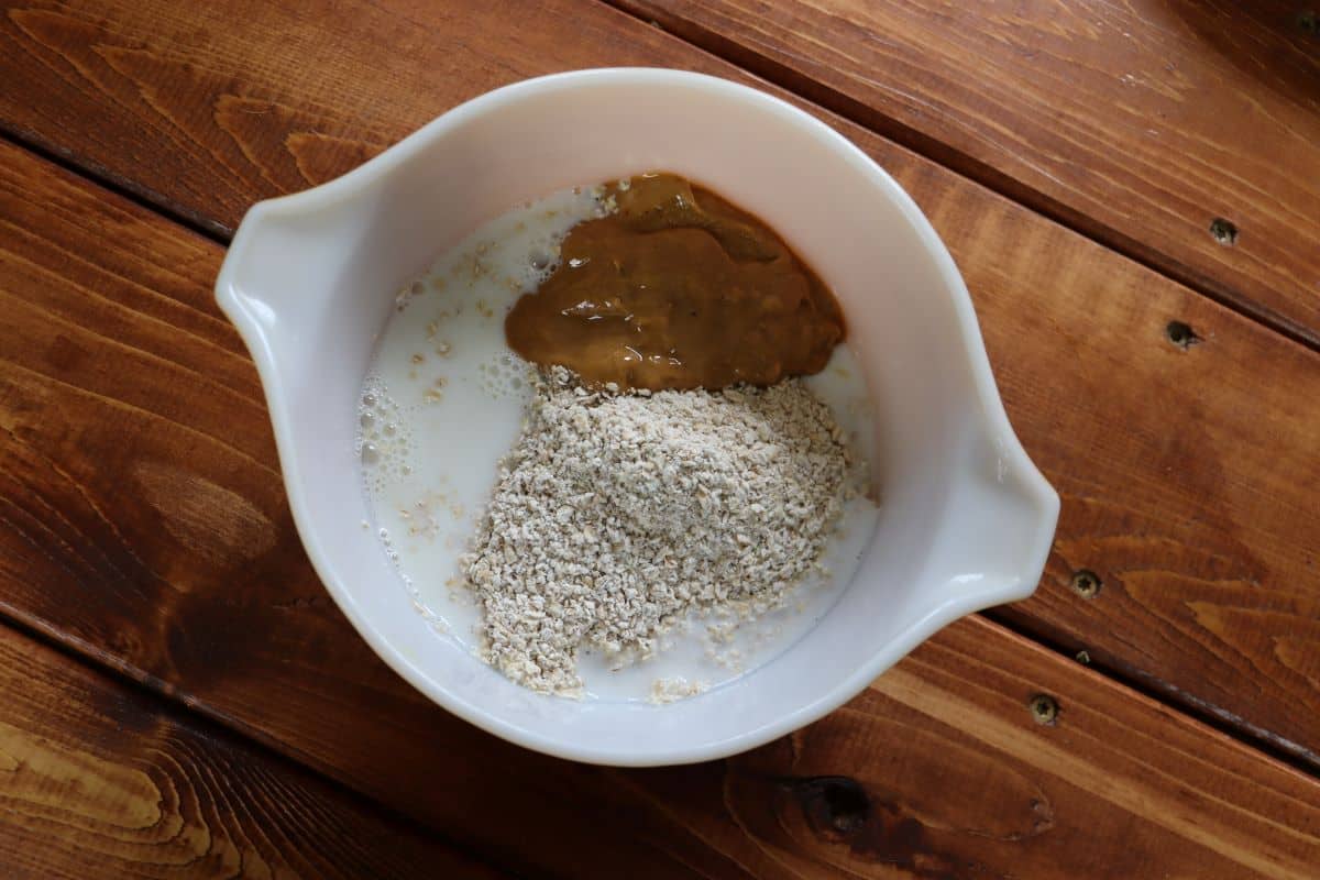Oat flour, peanut butter, and milk in a mixing bowl sitting on a wooden surface.