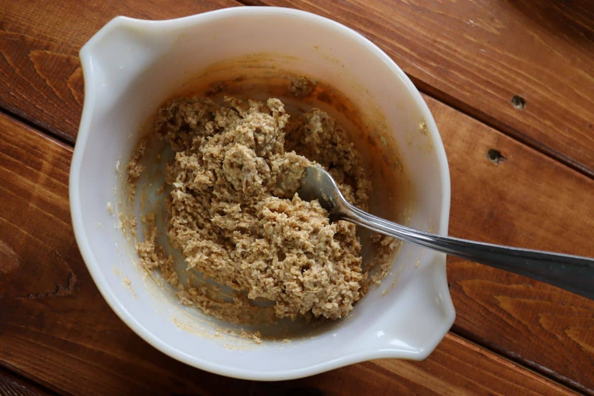 Light brown pasty dough in a mixing bowl with a fork in it sitting on a wooden surface.