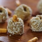 Oat-covered balls with yellow capsules partially inserted in the center, placed on a wooden surface; other capsules are scattered around the balls.