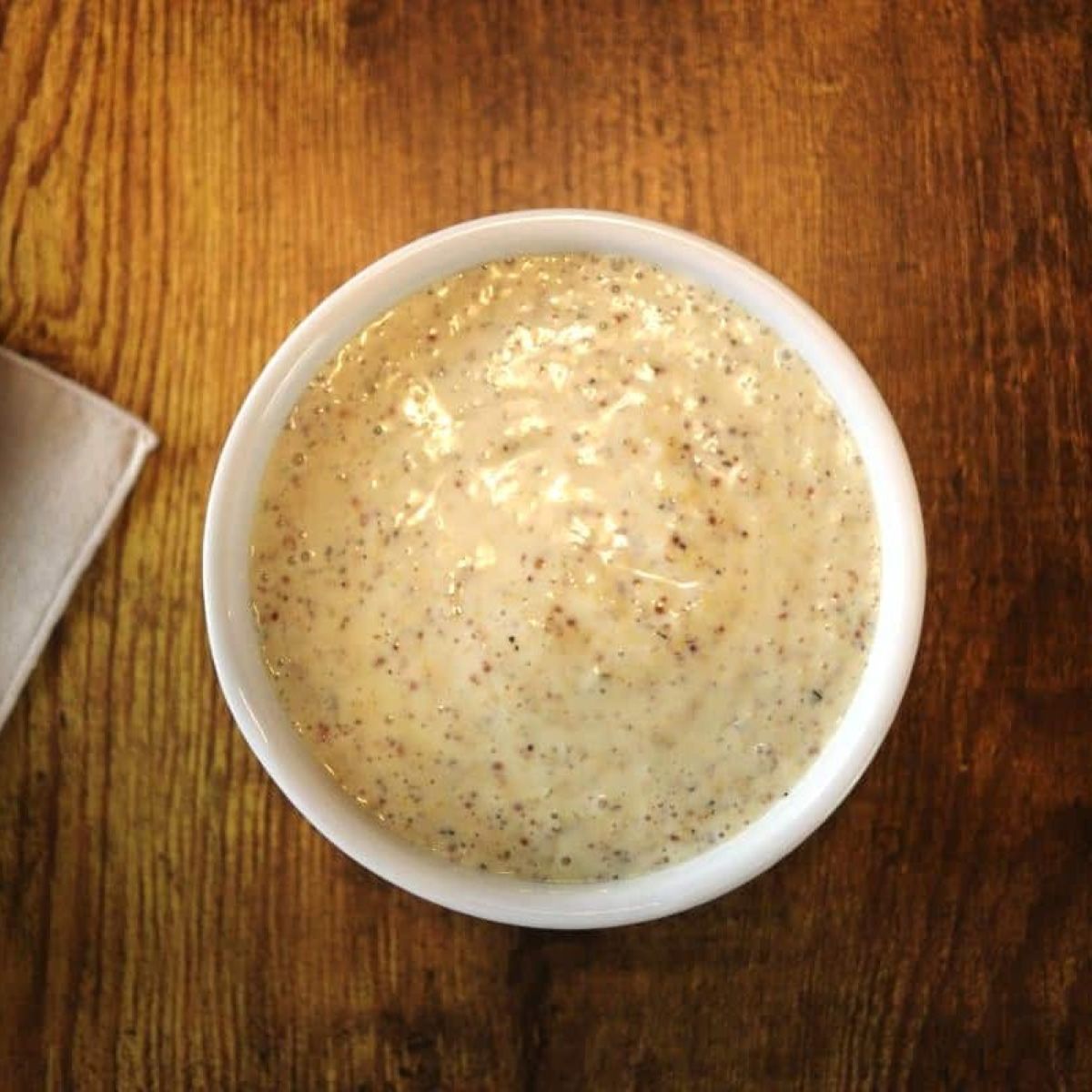 Grainy mustard sauce in a white dish on a wooden countertop.