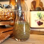 Tangy mustard salad dressing with herbs in a glass carafe on a kitchen counter.