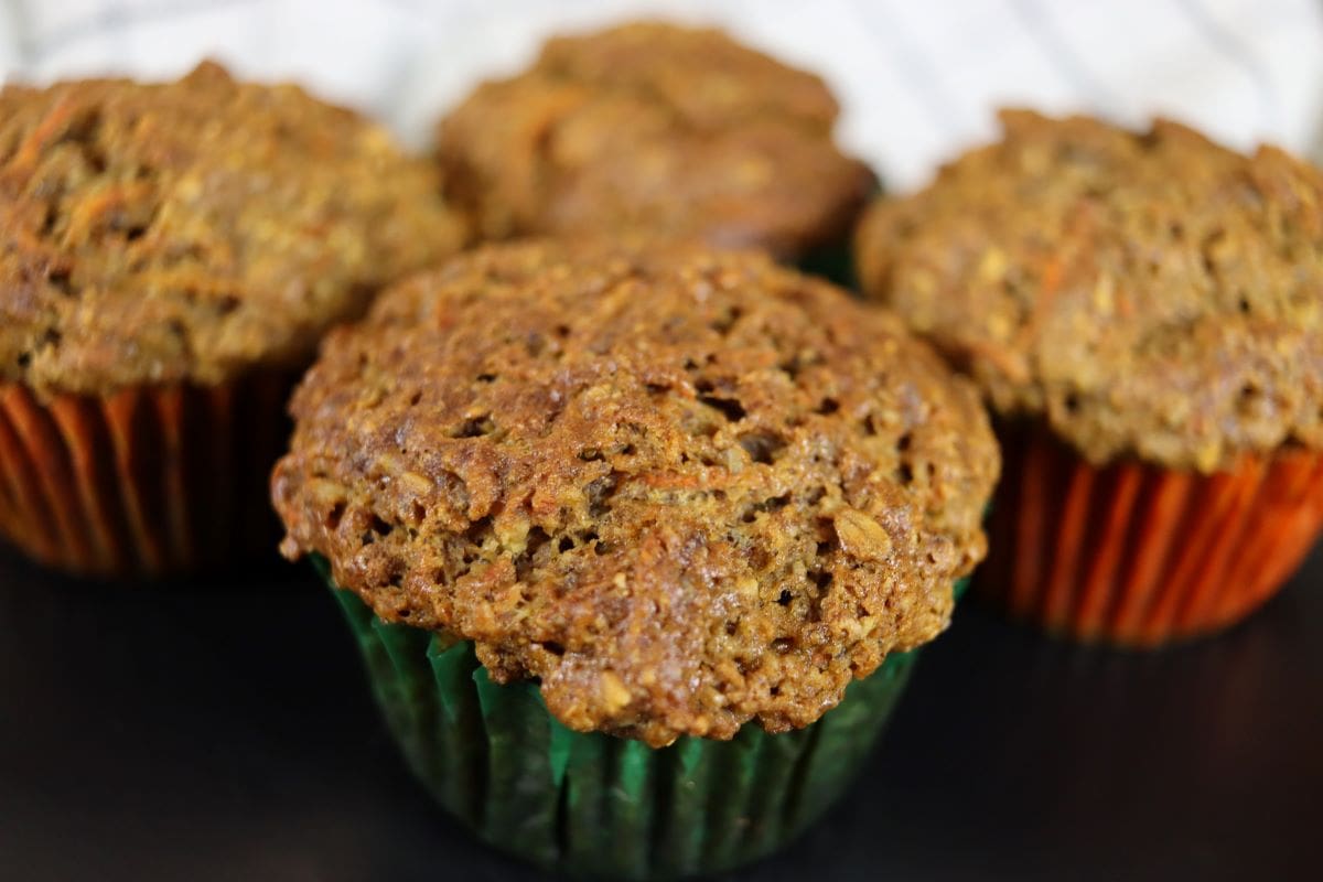 A golden brown carrot muffin with three others blurred in the background.