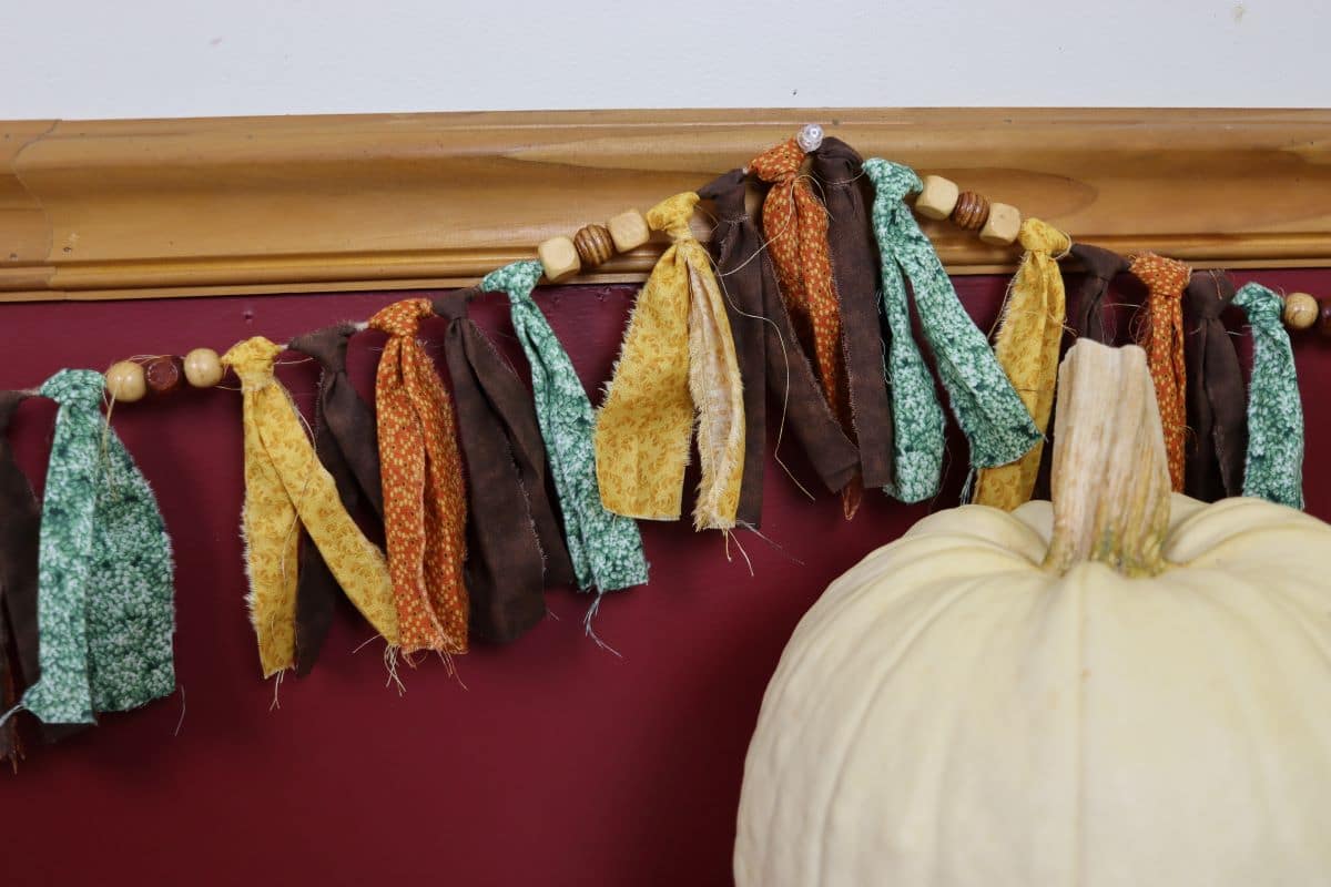 Homemade fall rag tie garland hanging on a wall behind a white pumpkin.
