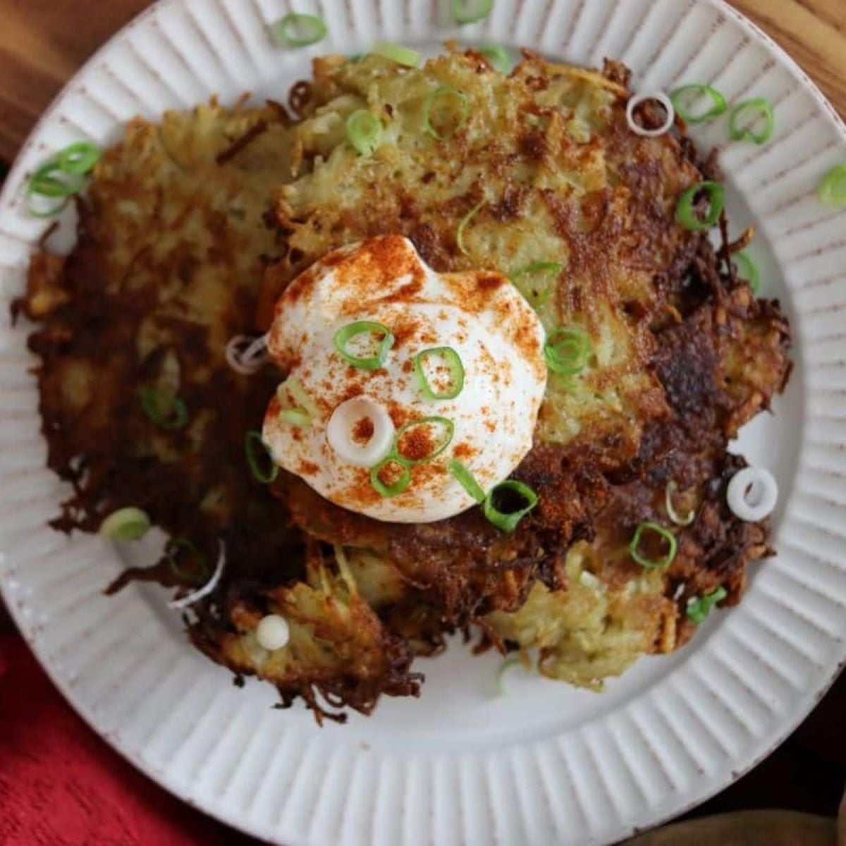 Stacked potato pancakes topped with sour cream, paprika, and sliced scallions on a white plate.