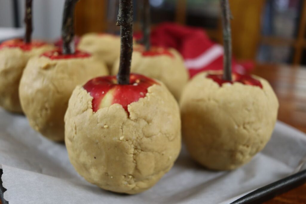 gourmet apples wrapped in peanut butter coating on a parchment lined sheet pan