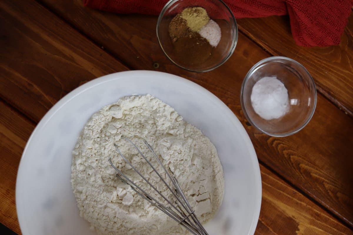 Bowls of flour, baking powder, and spices sit on a wooden surface.
