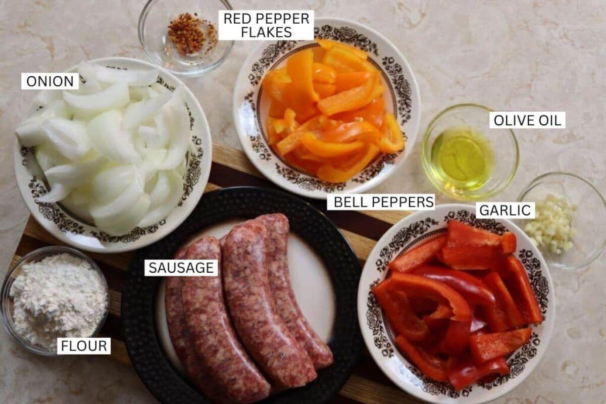 Ingredients for creamy sausage and pepper soup labeled sausage, bell peppers, onion, garlic, flour, olive oil, and red pepper flakes.
