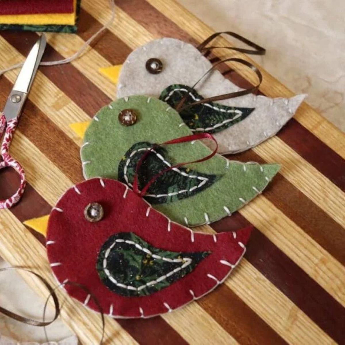 Three hand-sewnfelt bird ornaments in a vertical row on a striped wooden surface.