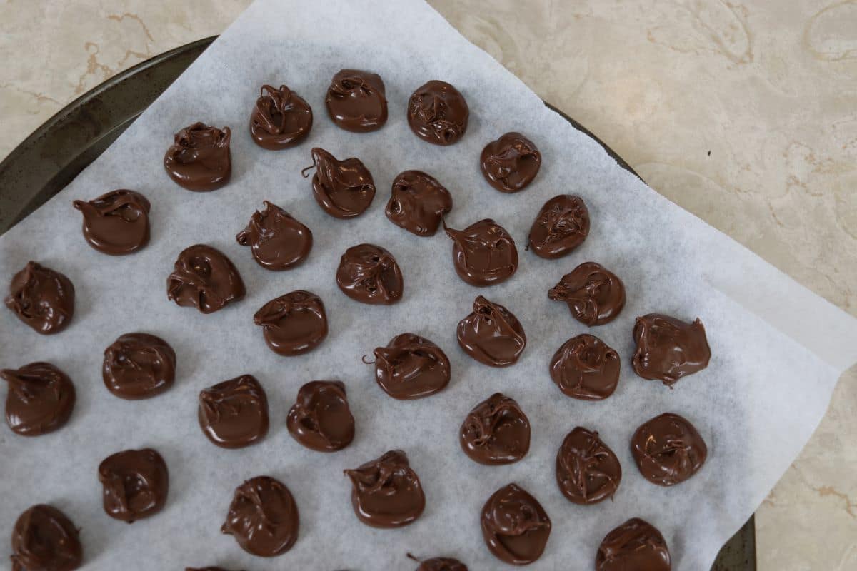 Drops of nutella on a parchment paper lined baking sheet.