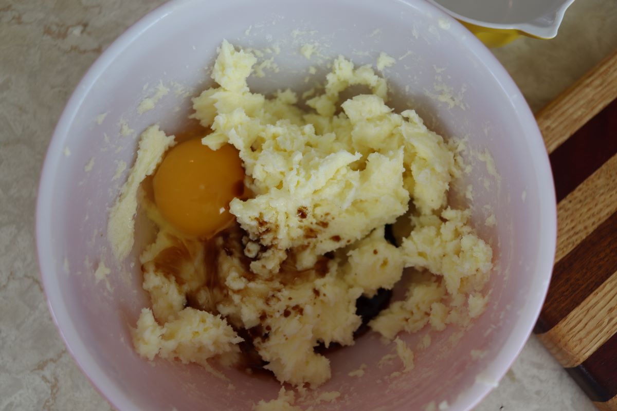 Creamed butter and sugar in a white bowl with dark spices and an egg in it.