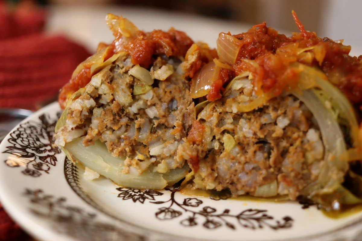 A stuffed cabbage roll on a plate topped with tomato sauce and shredded cabbage, served on a decorative dish with a fork and knife beside it.