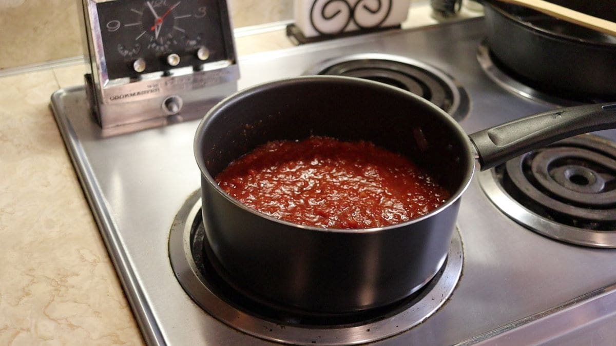 Saucepan full of tomato sauce sitting on a stovetop.