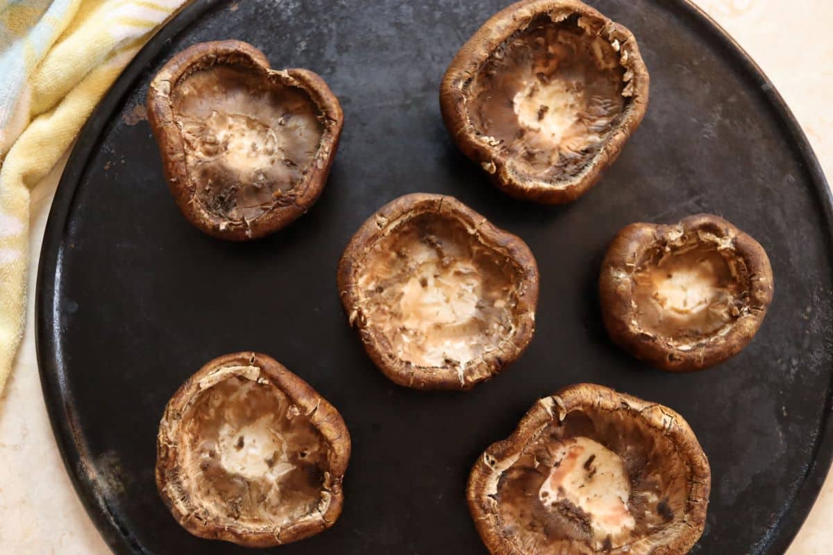 Mushroom caps with the stems and gills removed sitting on a dark stone baking tray.