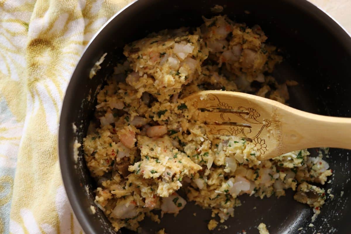 Stuffing with pieces of shrimp and fresh parsley visible in it in a pan with a wooden spoon.