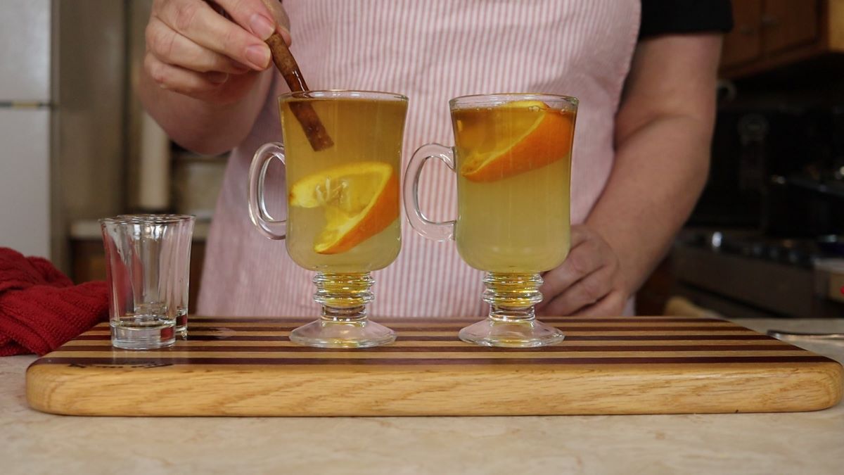 woman mixing a hot beverage in a glass cup with a cinnamon stick.