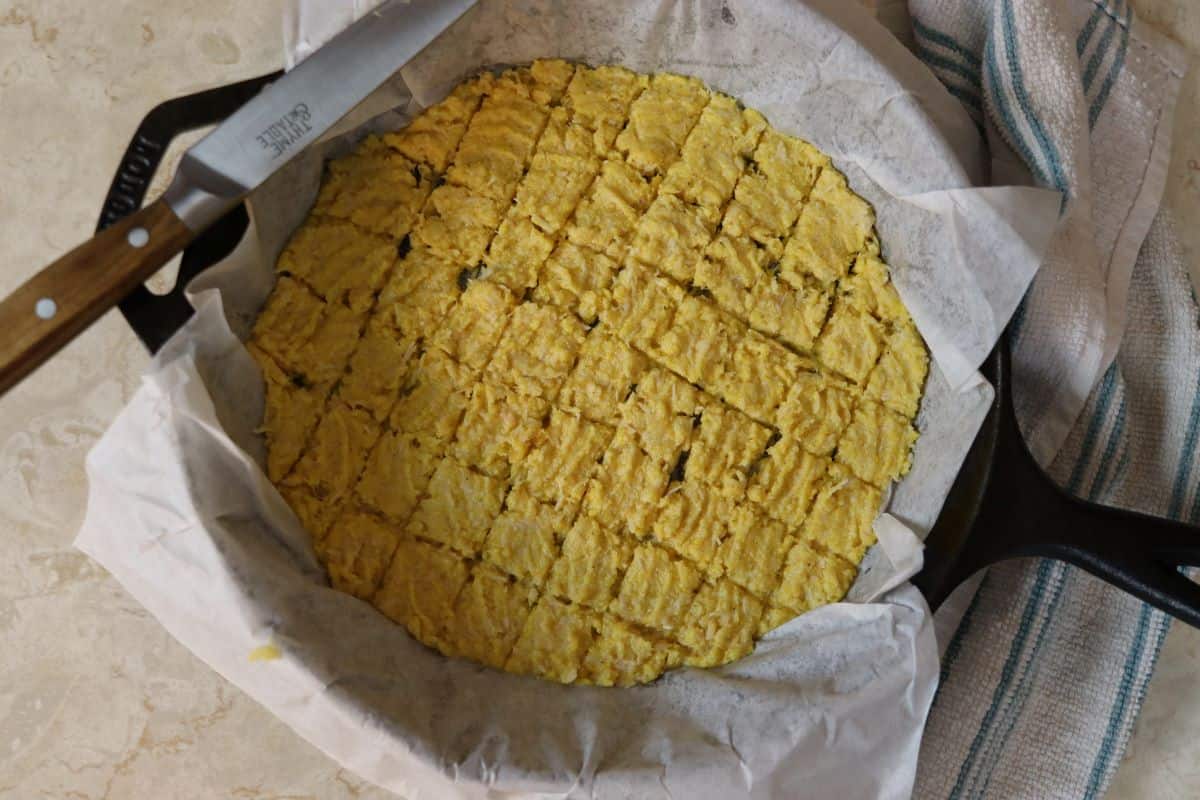 cast iron skillet lined with parchment paper with cat treat mixture spread evenly over the bottom and scored into little squares with a knife.