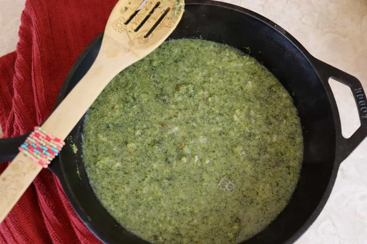 Pureed broccoli and broth in a cast iron dutch oven with a wooden spoon sitting on the edge of it.