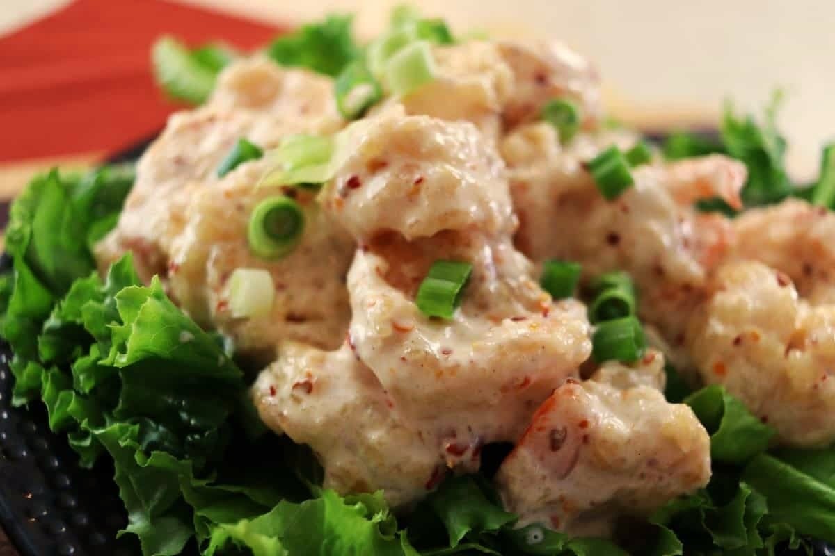 Creamy, sauced shrimp garnished with chopped green onions, served on a bed of fresh green lettuce leaves.