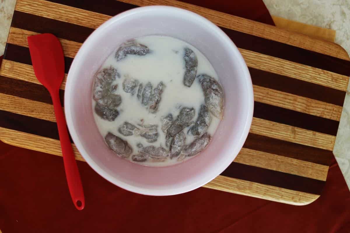 Shrimp in a bowl of buttermilk on a striped cutting board.