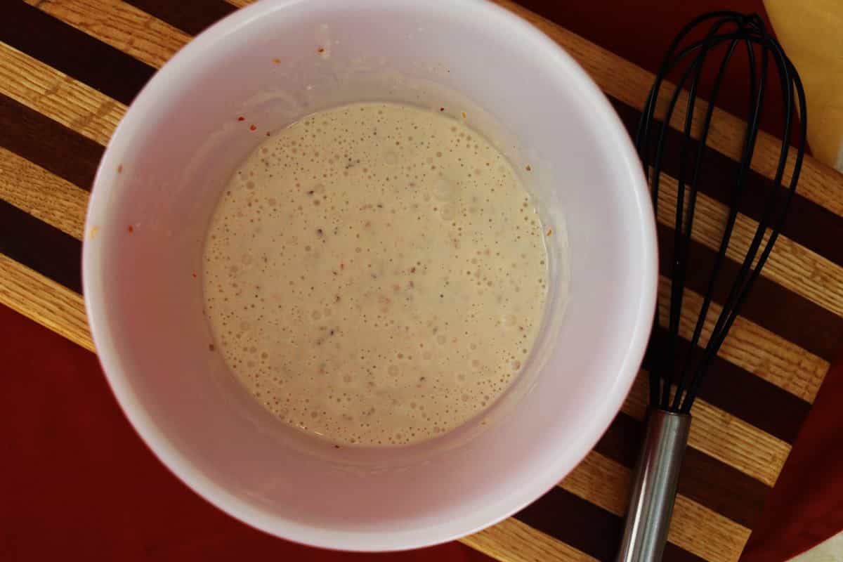 Light orange sauce in a white bowl sitting on a striped cutting board.