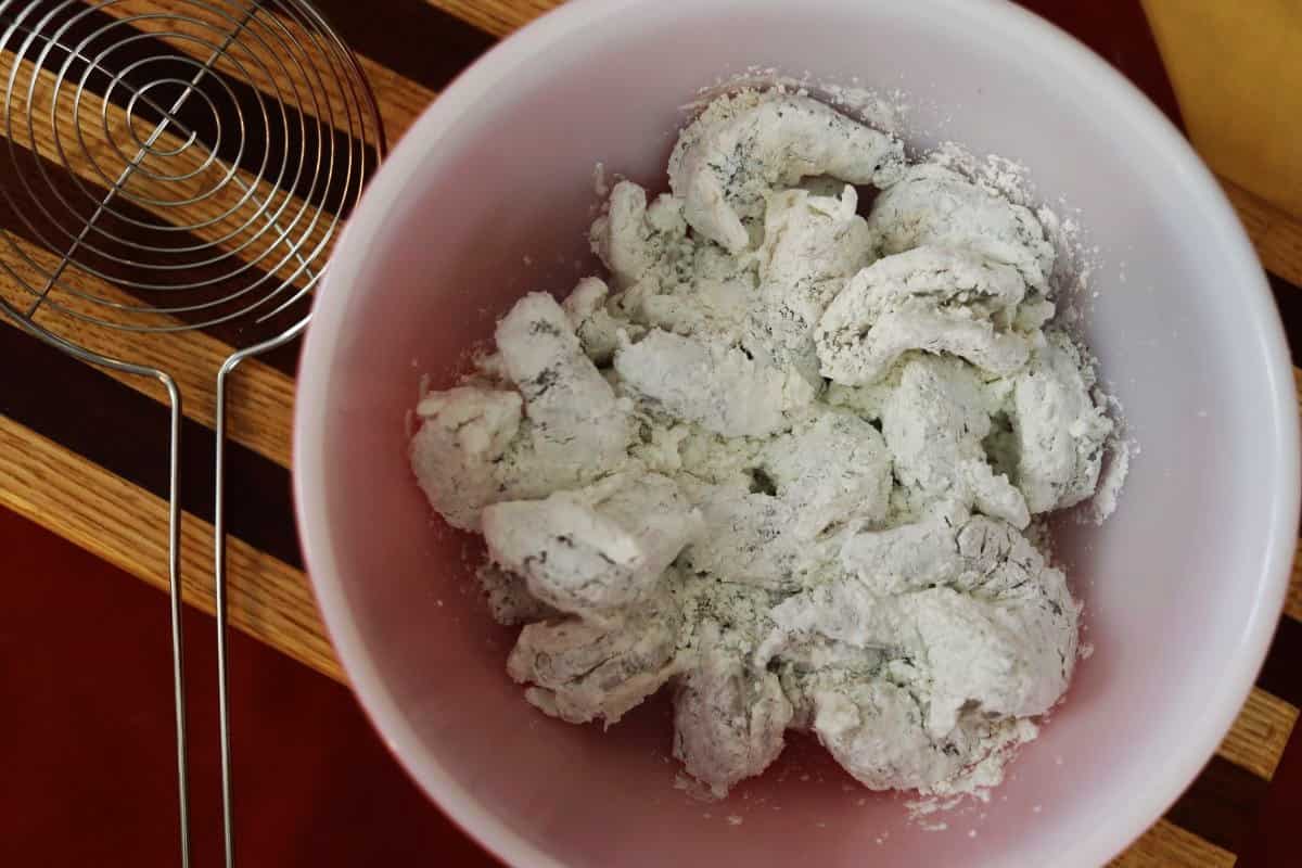 Shrimp coated in cornstarch in a white bowl on a striped cutting board.