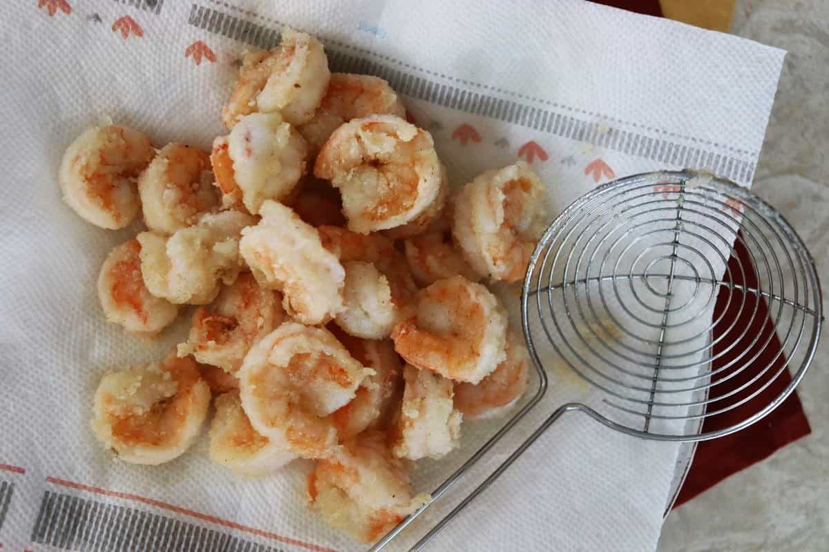 Fried shrimp sitting on a paper towel with a basket skimmer sitting next to it.