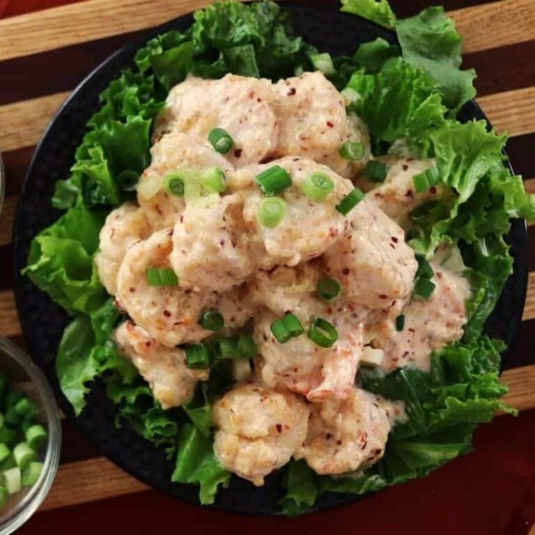 Shrimp covered in a creamy sauce garnished with chopped green onions, served on a bed of fresh green lettuce leaves.