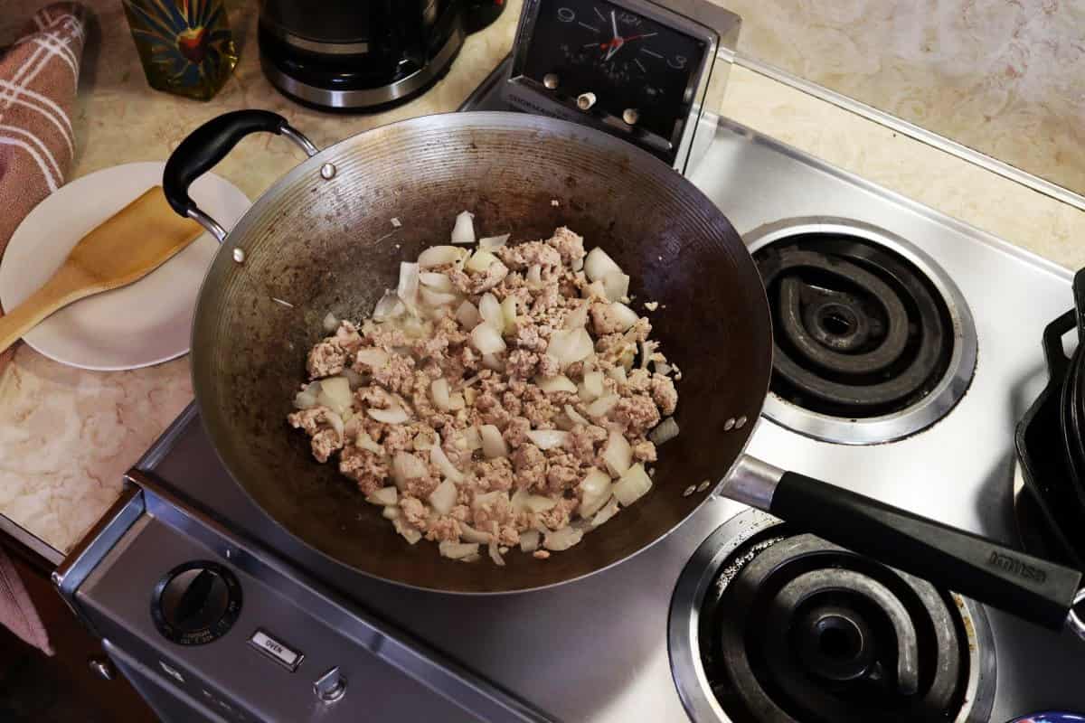 Wok on a stovetop with cooked ground pork and onions in it.